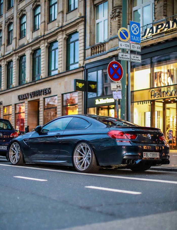 Black luxury sports car parked on a city street with urban architecture in the background.
